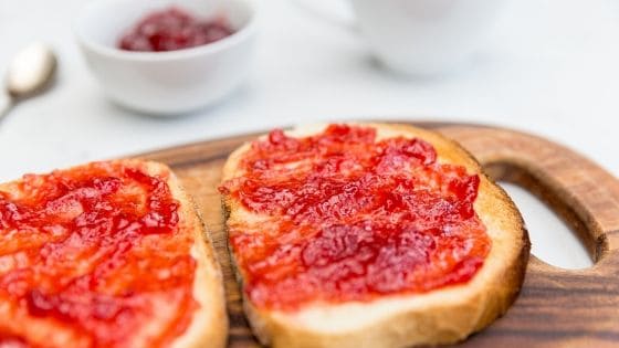 Toast mit Erdbeermarmelade auf Frühstücksbrett aus Holz
